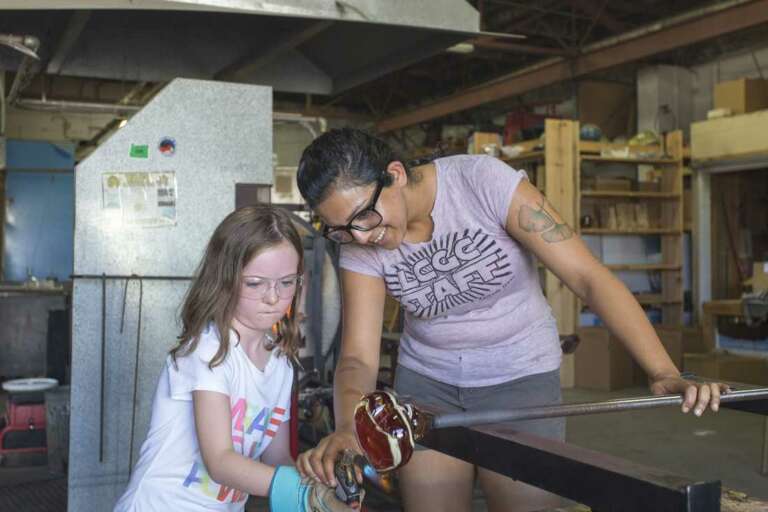 Glass artist blowing a glass float with young student